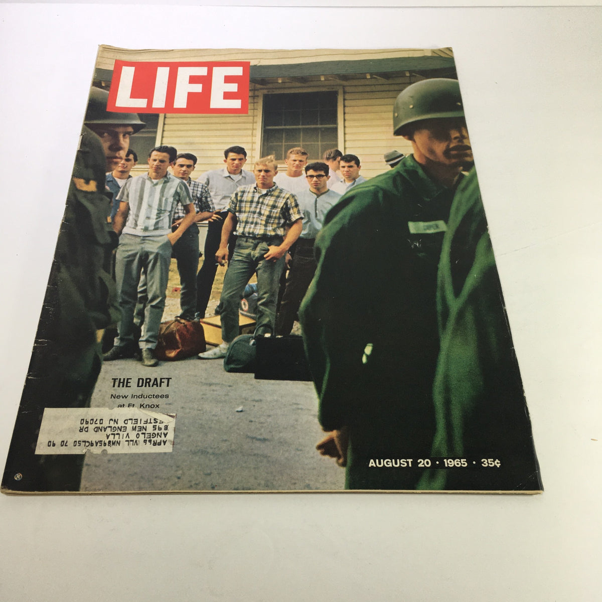 Cover of Life Magazine dated August 20, 1965, featuring the title 'The Draft: New Inductees at Ft Knox'. The image shows a group of young men gathered outside, with some wearing civilian clothes and others in military attire, reflecting the emotions and experiences of new inductees during the draft period.