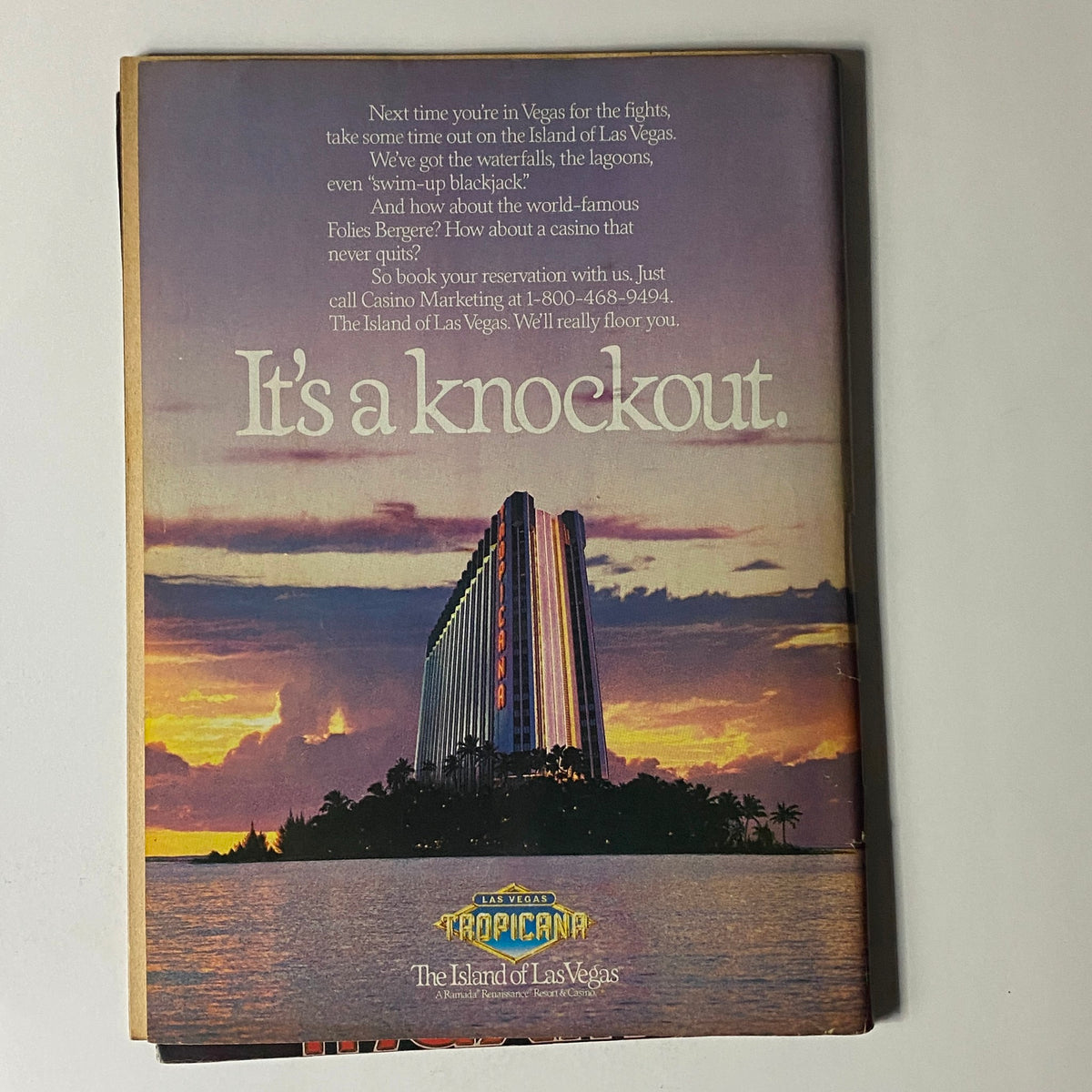 Back cover of Wrestling Fury Magazine December 1986 featuring an advertisement for the Las Vegas Tropicana. The image shows a colorful sunset over a tropical island with the memorable slogan "It's a knockout." This magazine features a classic wrestling rivalry between Hulk Hogan and Ric Flair and includes a collectible poster.