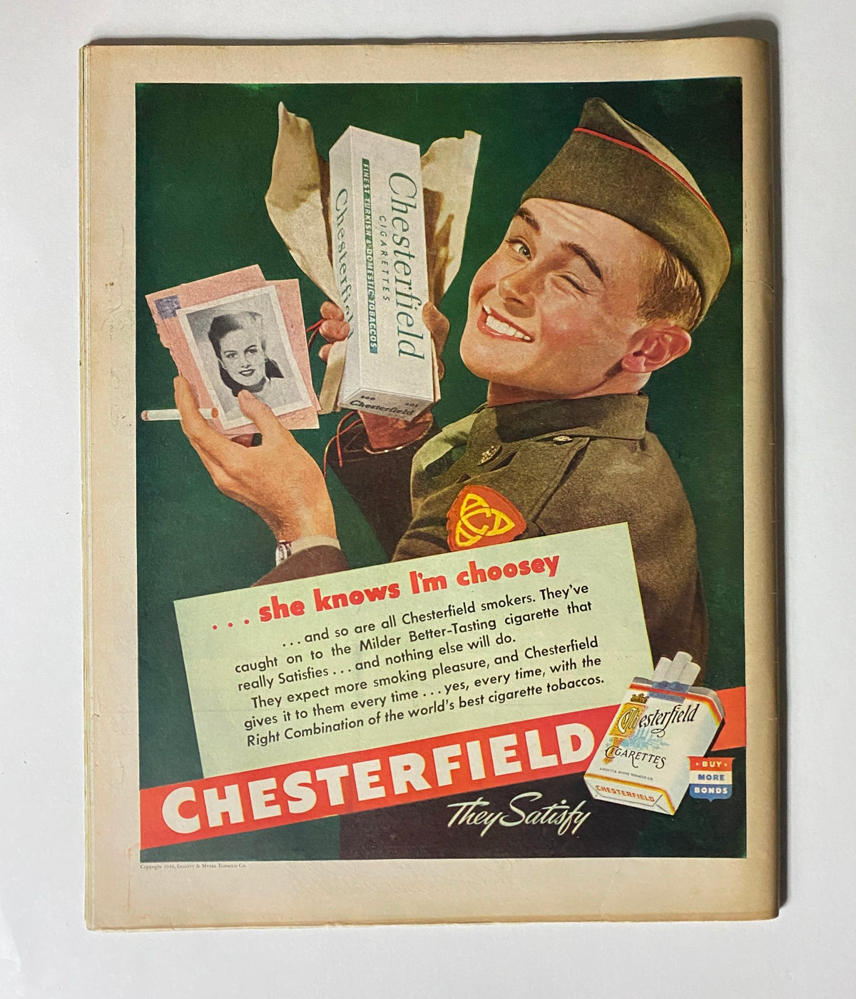 Vintage advertisement for Chesterfield cigarettes featuring a soldier smiling and holding cigarette packs, from VTG Collier's Magazine February 12, 1944, showcasing cultural elements of the 1940s.