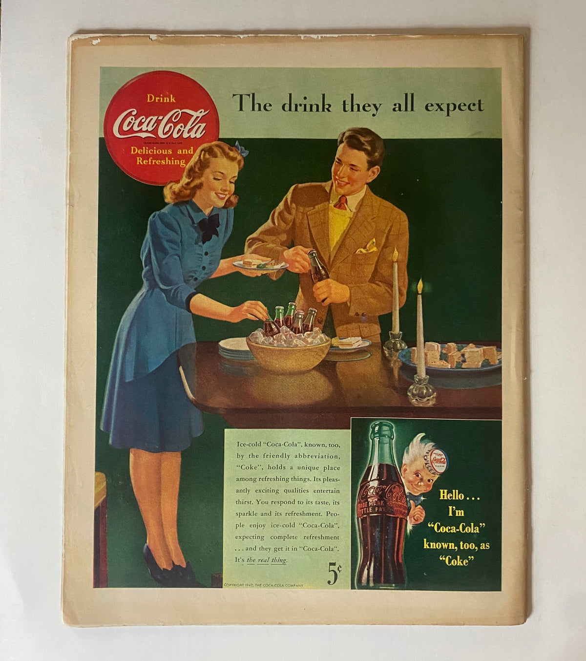 Vintage Coca-Cola advertisement featuring a young couple sharing drinks during a gathering. The article promotes Coca-Cola as the preferred refreshment. Highlights the tagline 'The drink they all expect' from the 1940s.