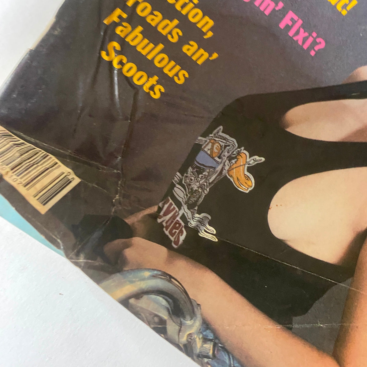Close-up section of the cover of VTG Easyriders Magazine August 1983 showing the model's tank top with motorcycle graphics, focusing on the headline 'Fiction, Broads an’ Fabulous Scoots'.