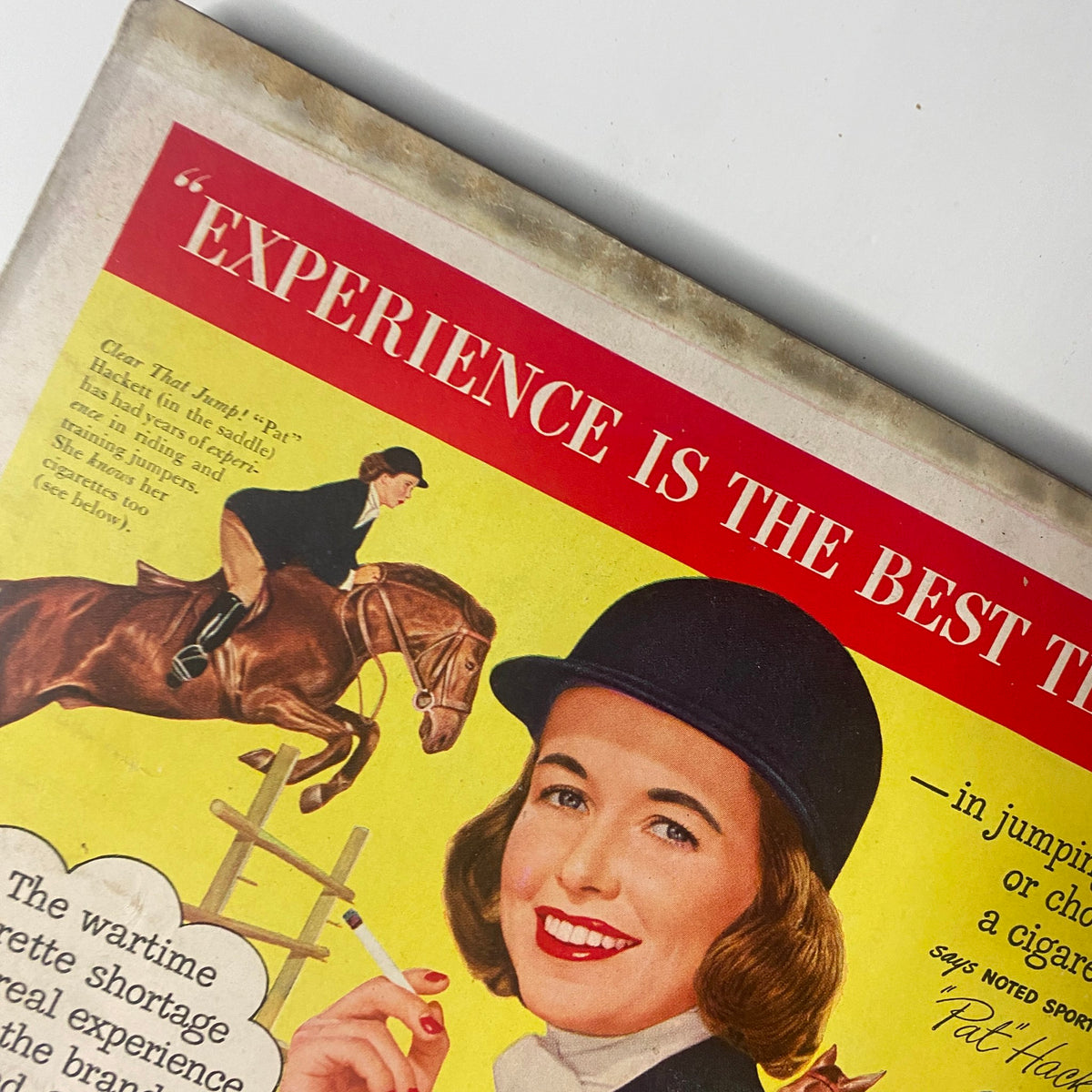 Close-up of the cover corner from Vogue Magazine October 1, 1947 highlighting a vintage advertisement featuring a woman smiling and holding a cigarette while riding a horse.