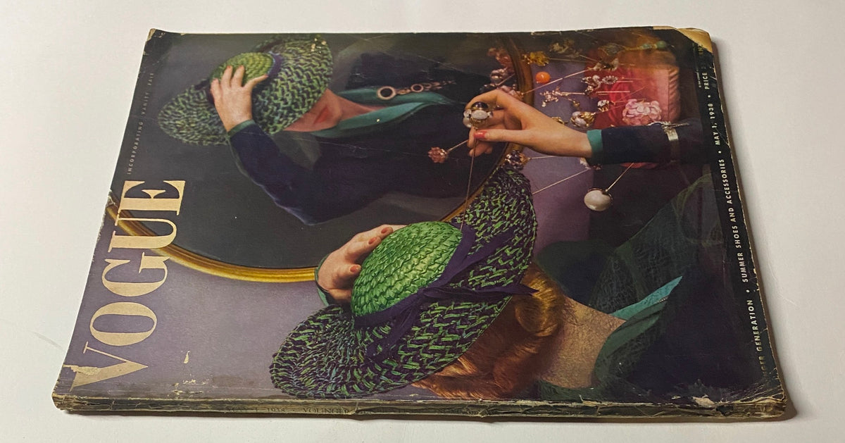 Vogue Magazine May 1, 1938 Cover displaying a close-up of a woman adjusting her green and purple hat, embodying classic 1930s fashion. This issue highlights floral arrangements and accessories, crafted by Anton Bruehl.