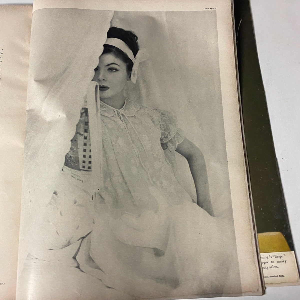 Vogue Magazine July 1957 Joanna McCormick Cover by Karen Radkai featuring a beautiful model partially hidden behind a curtain, dressed in elegant bridal attire.