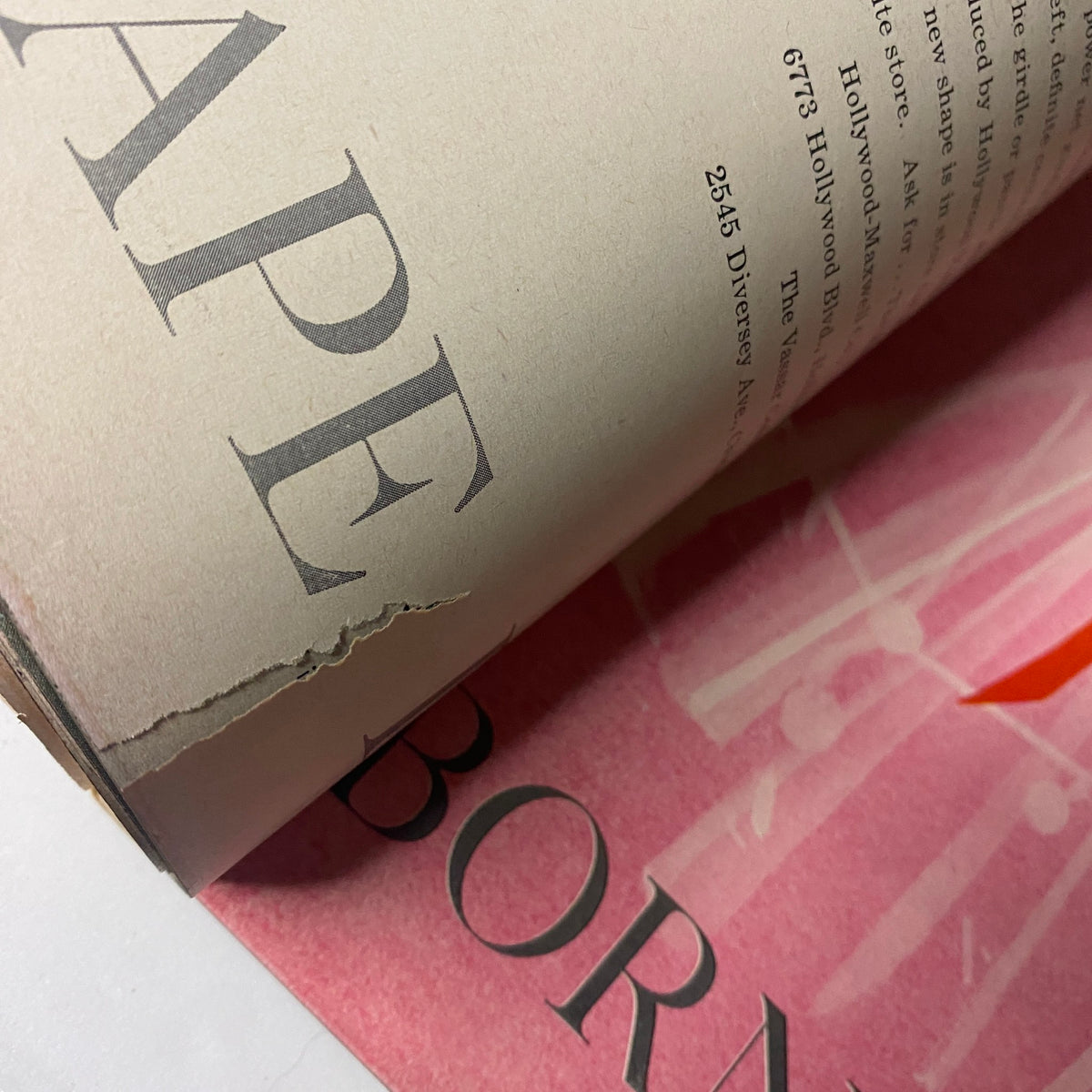 Vogue Magazine October 1, 1957 Mary McLaughlin Cover by William Klein, capturing a close-up of a magazine page showing text with a tear, indicating the vintage condition of the magazine.