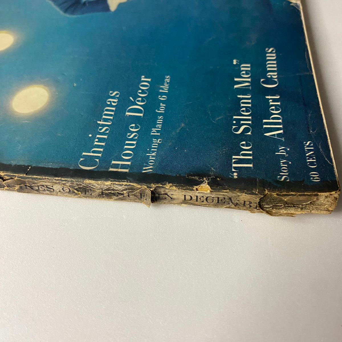 Close-up of the damaged spine of Vogue Magazine December 1957 featuring Gyongyi Armstrong on the cover, photographed by Karen Radkai. Highlights vintage wear including binding wear and corner damage.
