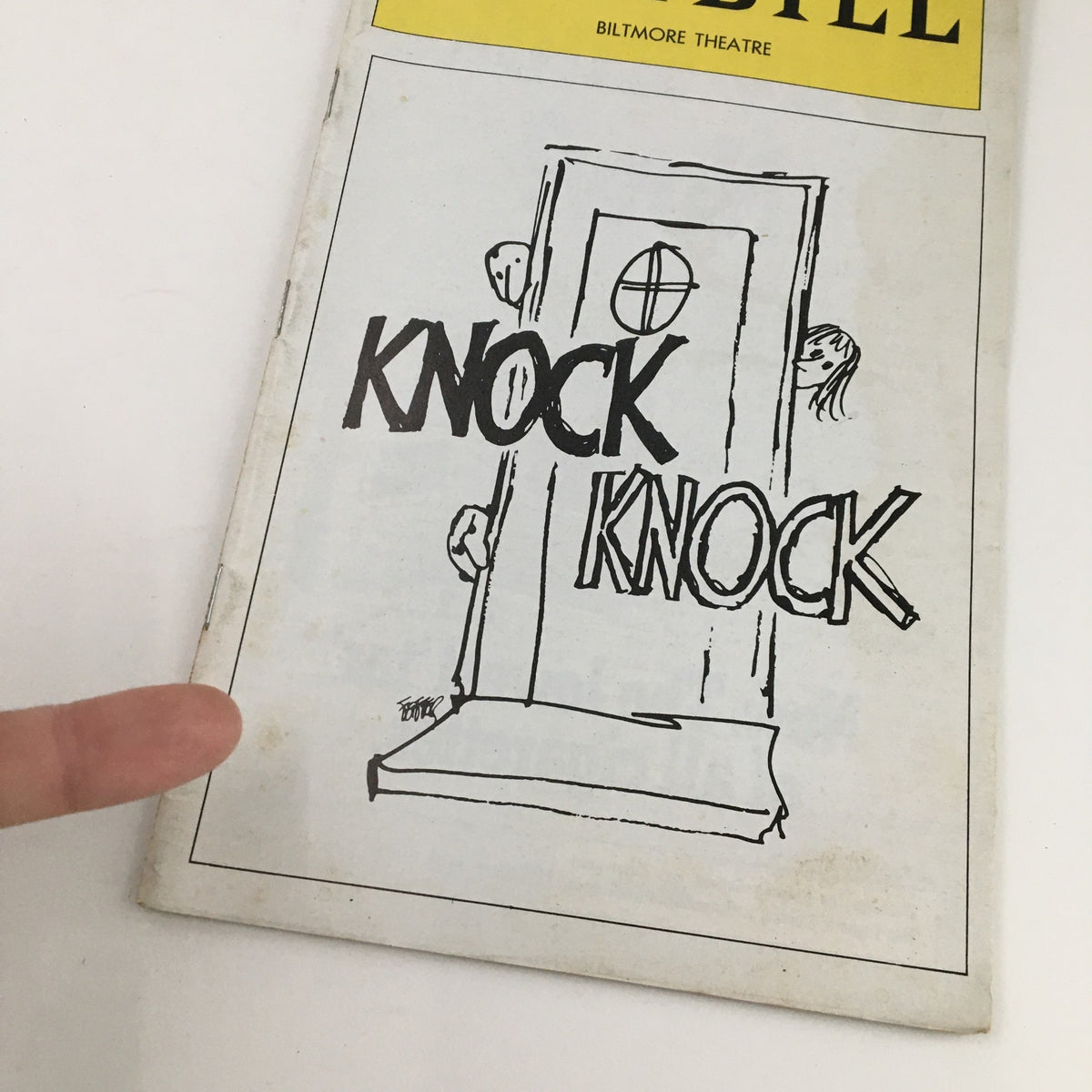 Close-up view of the 1976 Playbill from Biltmore Theatre for Jules Feiffer's 'Knock Knock', highlighting the illustrated cover with the title and a finger pointing at the design.