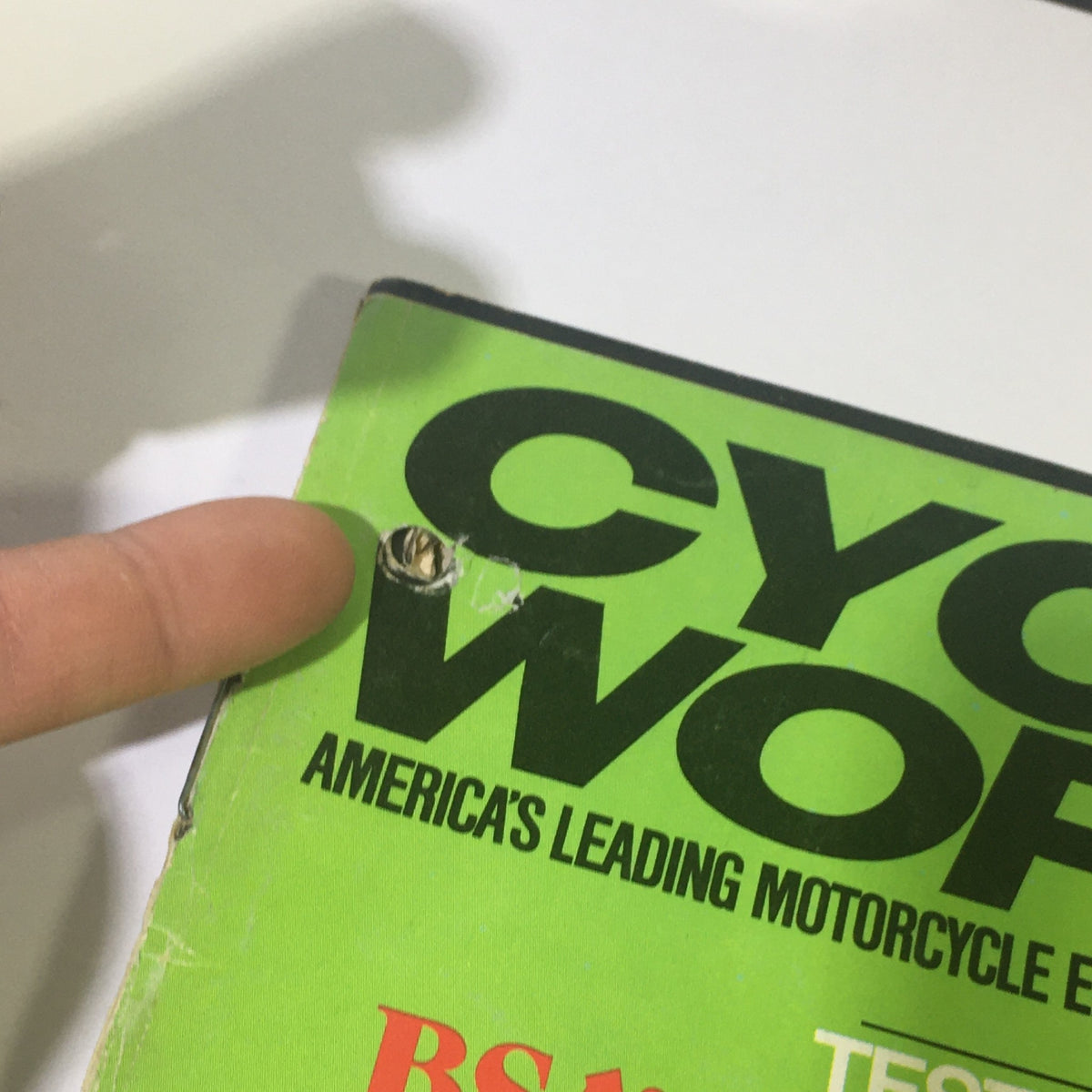 Examination of the spine area of Cycle World Magazine January 1972, showing signs of aging, including a small hole, reflecting its history and collectibility.
