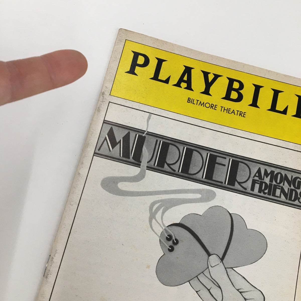 Close-up view of the 1975 Playbill Biltmore Theatre for Murder Among Friends, highlighting the cover art and details with a finger pointing at it.