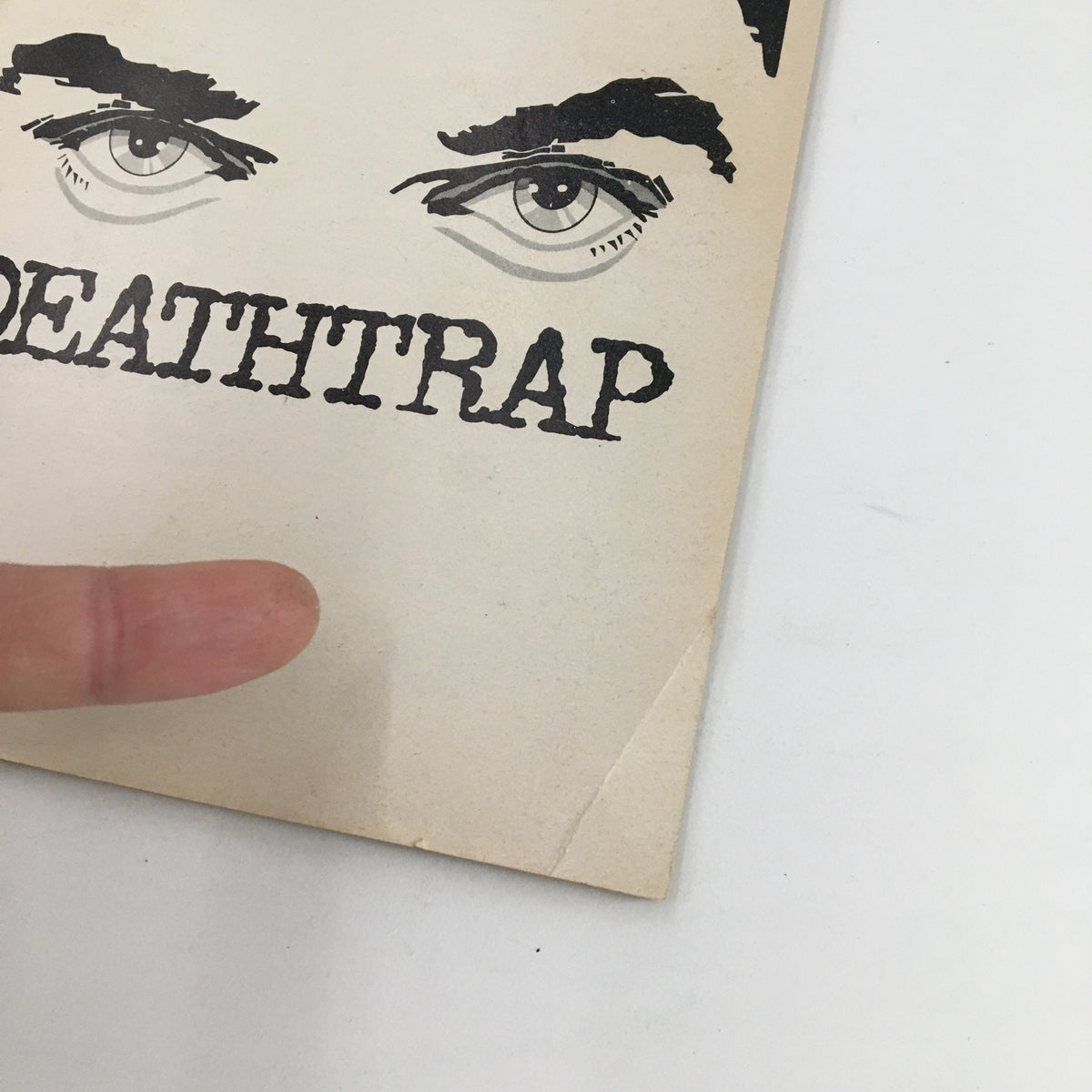 Close-up view of the cover of the 1978 Playbill for The Music Box production of John Wood in Ira Levin's Deathtrap, featuring the title art with a finger in the frame.