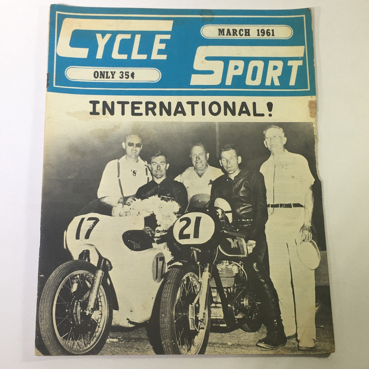 Cover of VTG Cycle Sport Magazine March 1961 featuring international race theme, showcasing men beside vintage racing motorcycles.