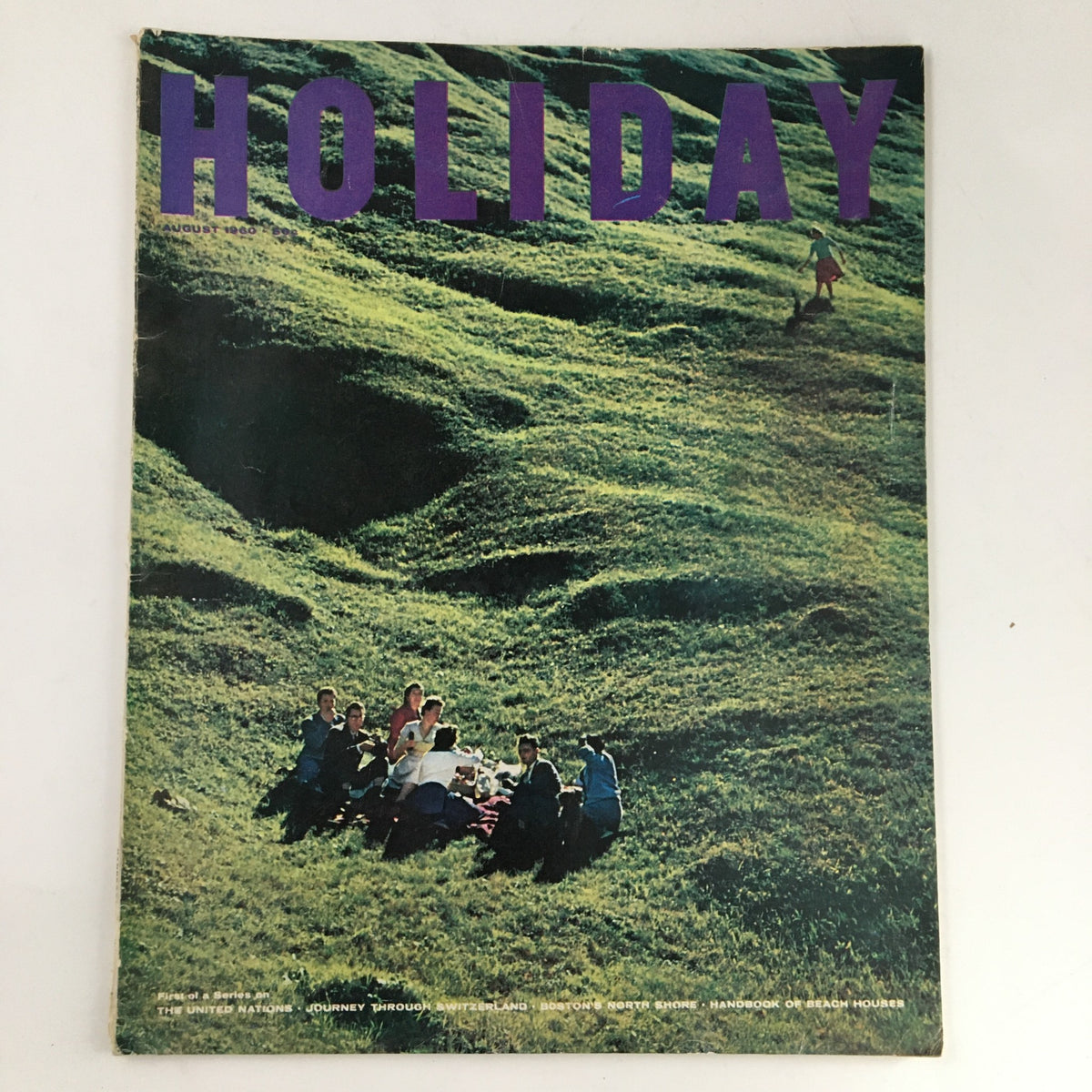 Cover of Holiday Magazine August 1960 featuring a scenic image of people enjoying nature in Switzerland with vibrant green hills, highlighting the issue's journey through Switzerland.