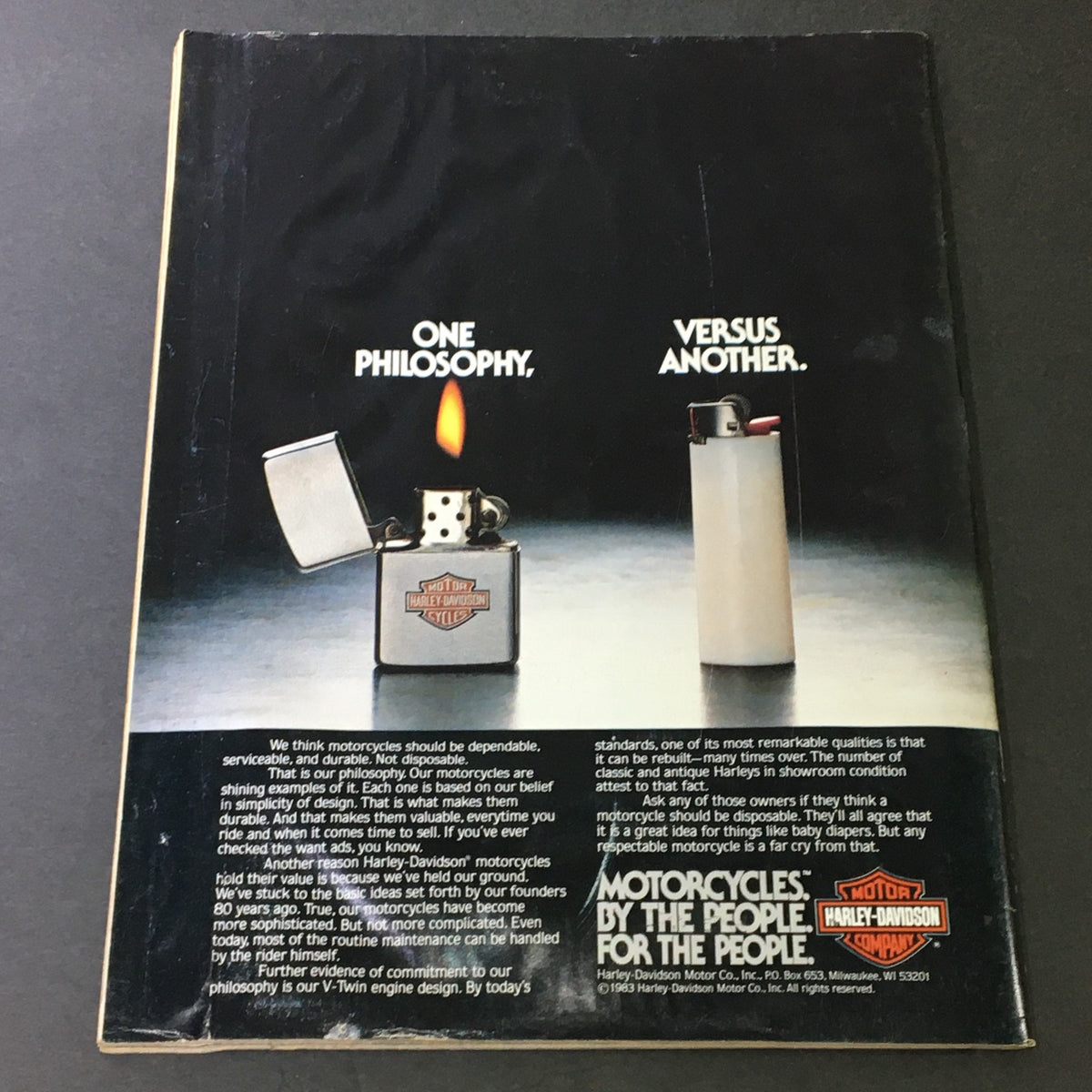 Back cover of VTG Cycle Magazine January 1983 featuring a comparison advertisement between Harley-Davidson and other motorcycle philosophies, showcasing a lit lighter and a plain lighter, emphasizing Harley-Davidson's commitment to durability and serviceability.