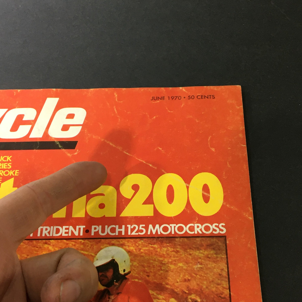 Close-up of the June 1970 Cycle Magazine cover showcasing the title 'Daytona 200' along with features on Triumph Trident and Punch 125. A finger points to the title on a vibrant orange background.