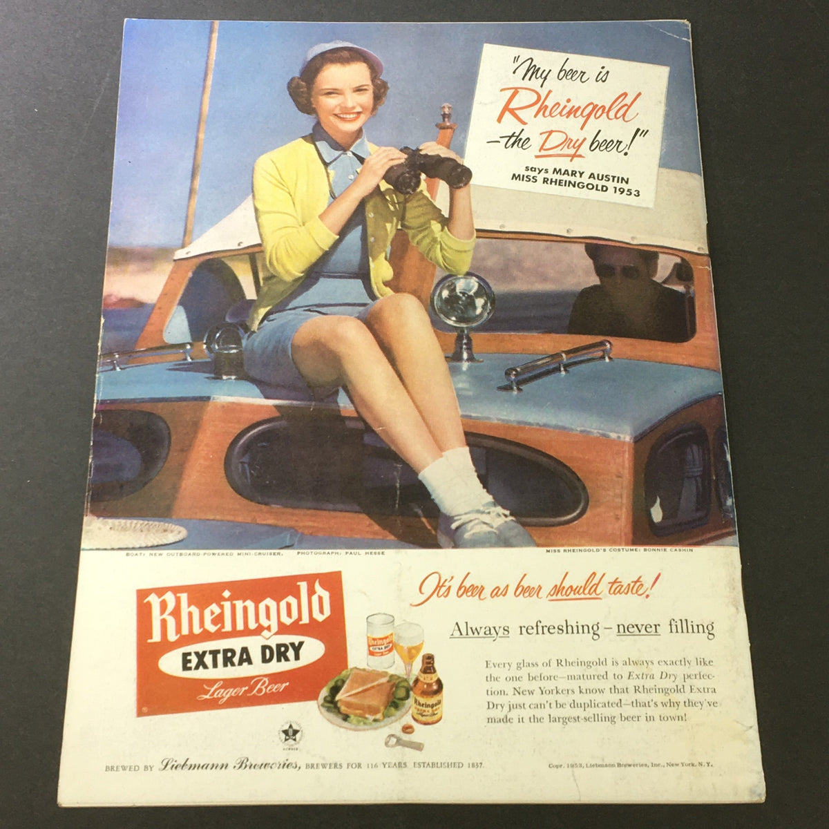 Vintage advertisement for Rheingold Extra Dry Lager Beer featuring Miss Rheingold 1953, showcasing a joyful woman with binoculars sitting on a retro boat, promoting the beer's refreshing qualities.