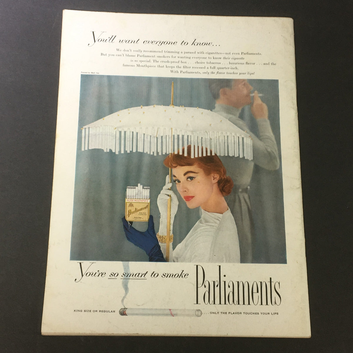 Back cover of a vintage advertisement for Parliaments cigarettes, showcasing a stylish woman with an umbrella and a pack of cigarettes, capturing mid-20th century advertising trends.