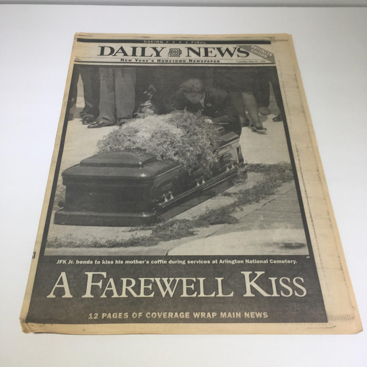 NY Daily News newspaper front page from May 24, 1994, featuring the headline 'A Farewell Kiss' and an image of JFK Jr. bending to kiss his mother's coffin during memorial services at Arlington National Cemetery.