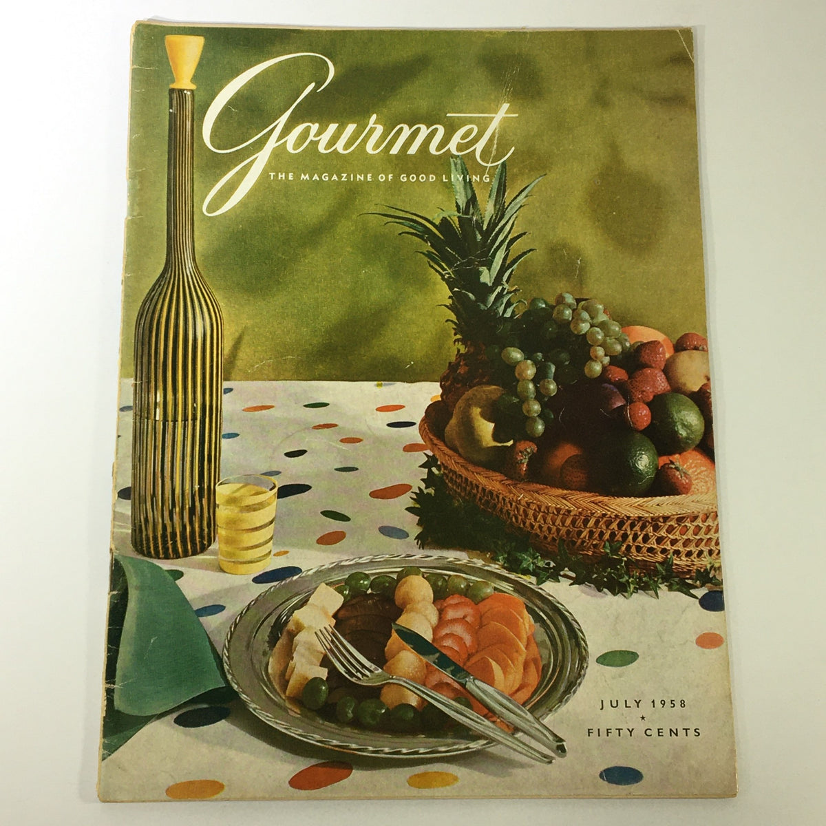 Cover of VTG Gourmet The Magazine of Good Living July 1958 - High-Style Barbecue featuring a vibrant table setting with a plate of assorted foods, fruits, and a decorative background.