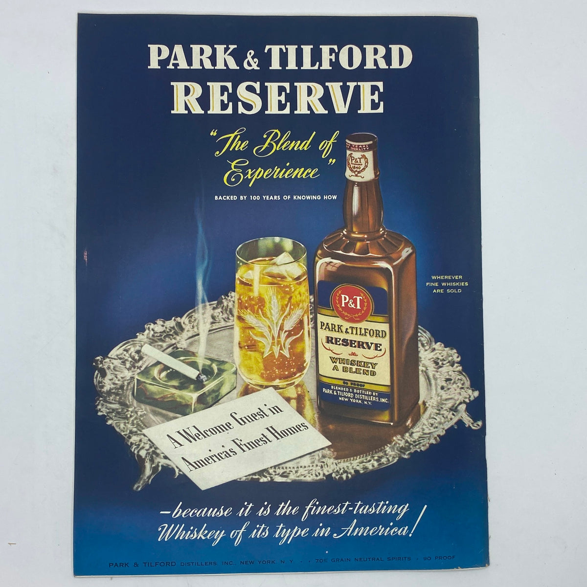 Park & Tilford Reserve Whiskey vintage advertisement featuring the slogan 'The Blend of Experience.' The image showcases a bottle of Park & Tilford Reserve, a glass with a drink, and an accompanying note, all set on an elegant serving tray.