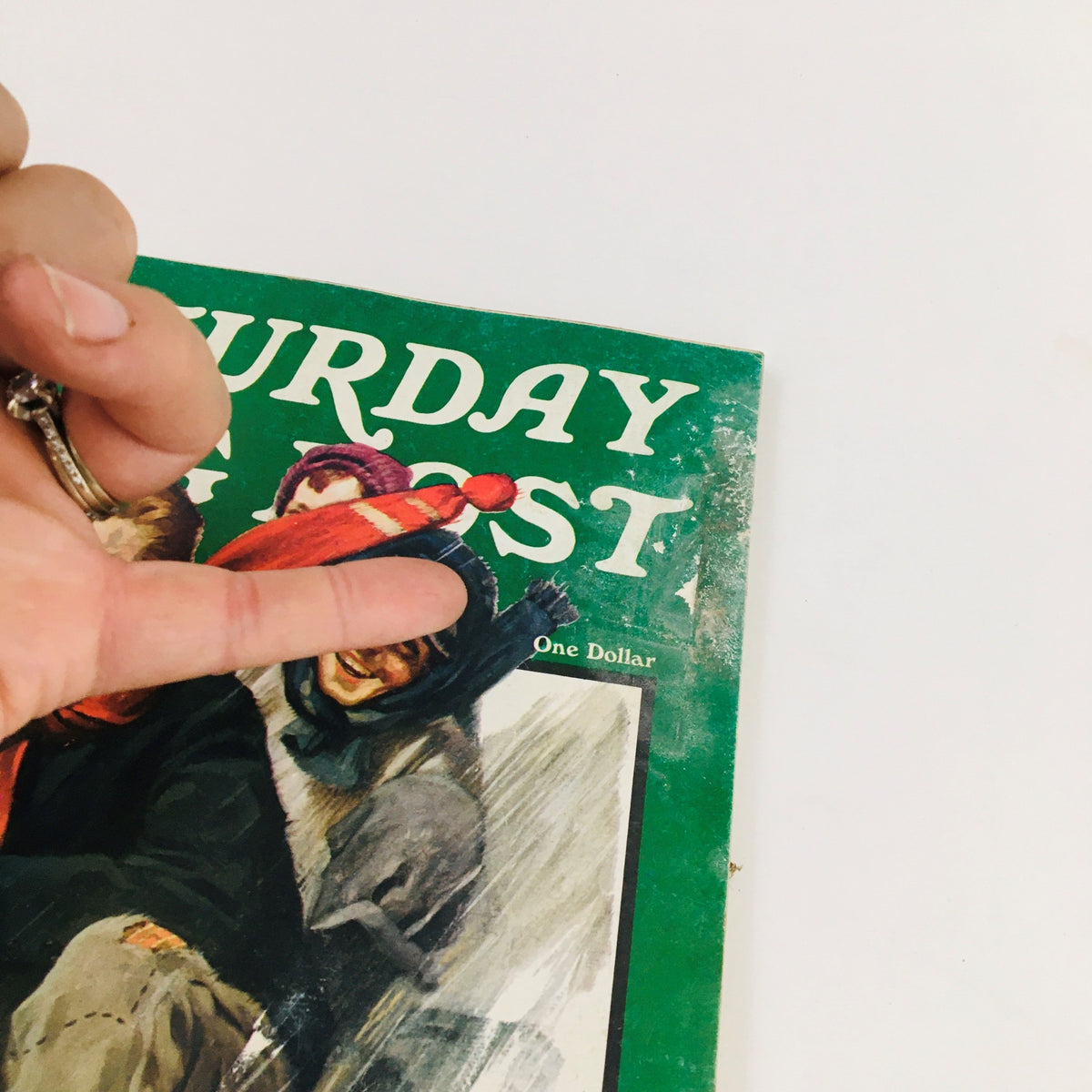 Close-up of the cover of The Saturday Evening Post Winter 1973 showing a hand pointing at the title, with children and a dog depicted in a winter scene.