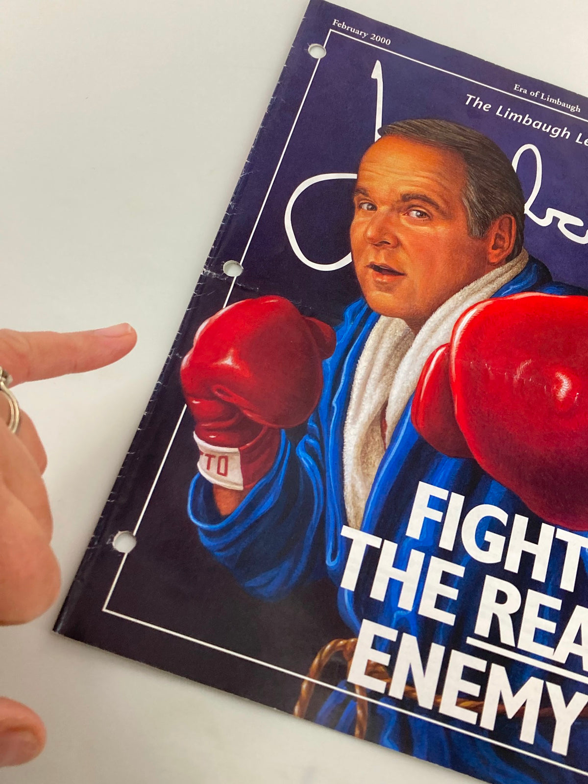 Detail view of the Rush Limbaugh Letter Newsletter Magazine from February 2000 titled 'Fight The Real Enemy', showing the cover and a hand pointing at it for emphasis.