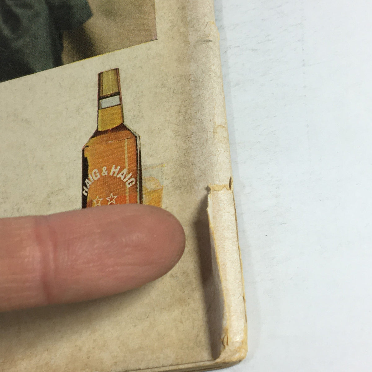 Close-up view of the edge of the VTG Gourmet Magazine Cover from October 1965, showcasing minor wear and a vintage bottle of Haig & Haig whiskey.