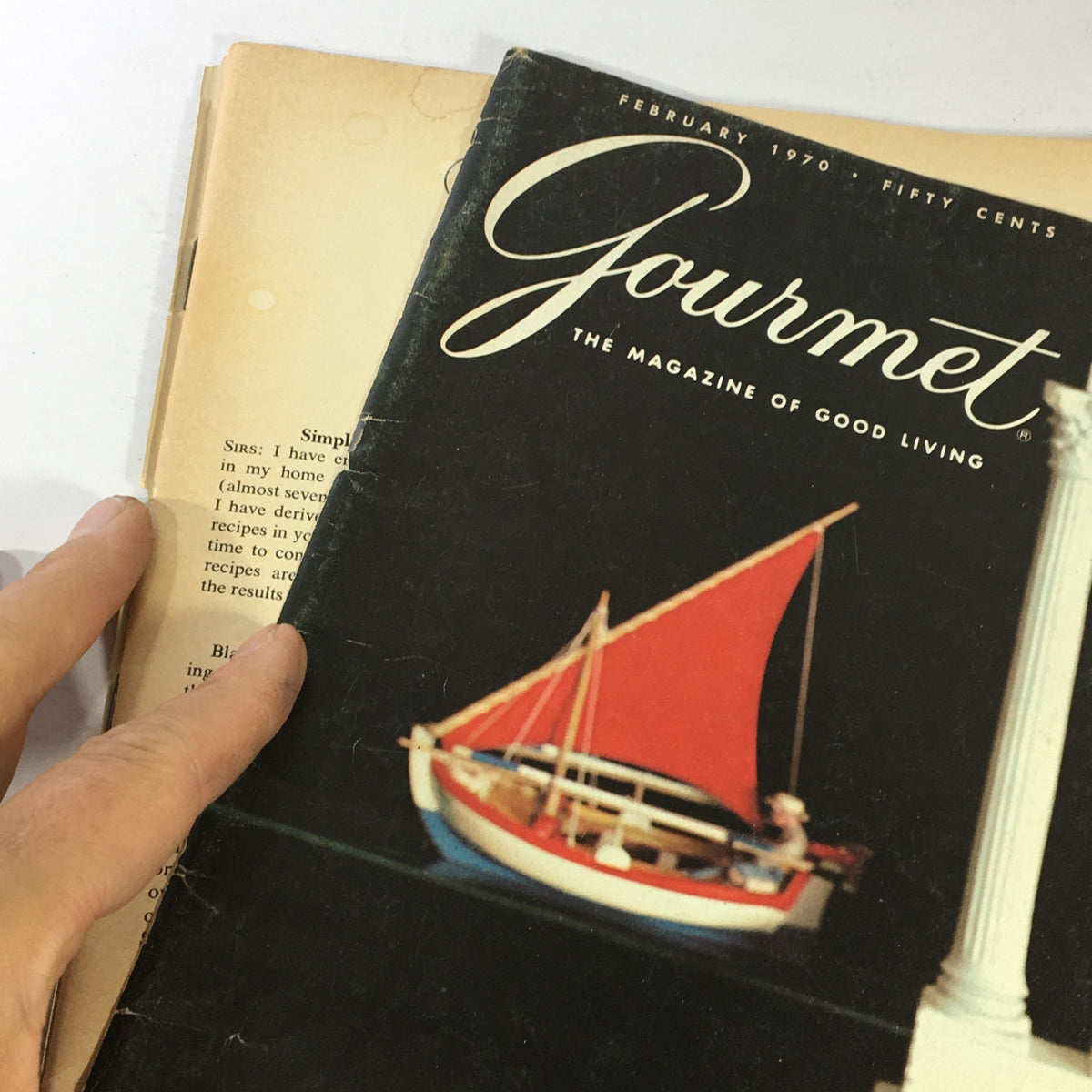 Close-up of the cover of VTG Gourmet The Magazine of Good Living February 1970, showcasing a model sailboat and an elegant design, highlighting the magazine's focus on culinary culture.