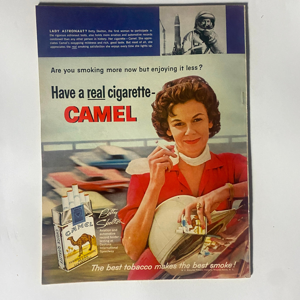 Vintage advertisement featuring a woman promoting Camel cigarettes in a retro style, with the text 'Have a real cigarette - CAMEL'. The image reflects mid-20th century marketing and automotive culture, linked to the VTG Motor Trend Magazine August 1961 Chevy & Ford Six & V-8 Tests.