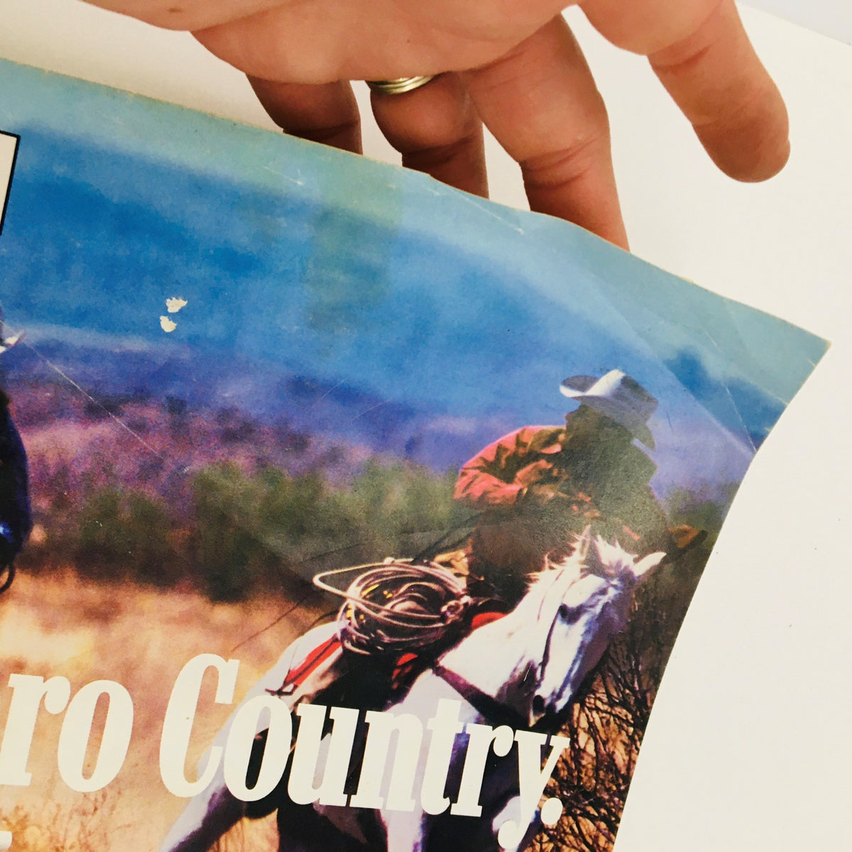 Hand holding the edge of the Marlboro brochure depicting cowboys and the text 'Come to Marlboro Country'.