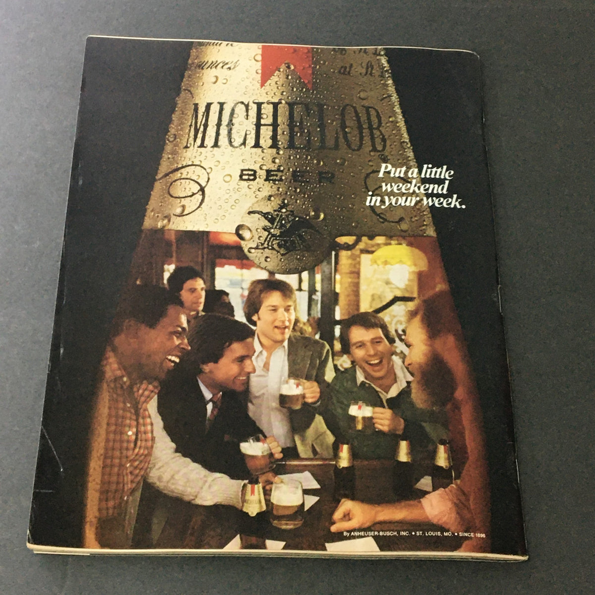 Back cover of a vintage Sports Illustrated magazine, featuring a group of men enjoying drinks at a bar, promoting Michelob beer with the slogan 'Put a little weekend in your week', adding a social touch to the sports magazine.