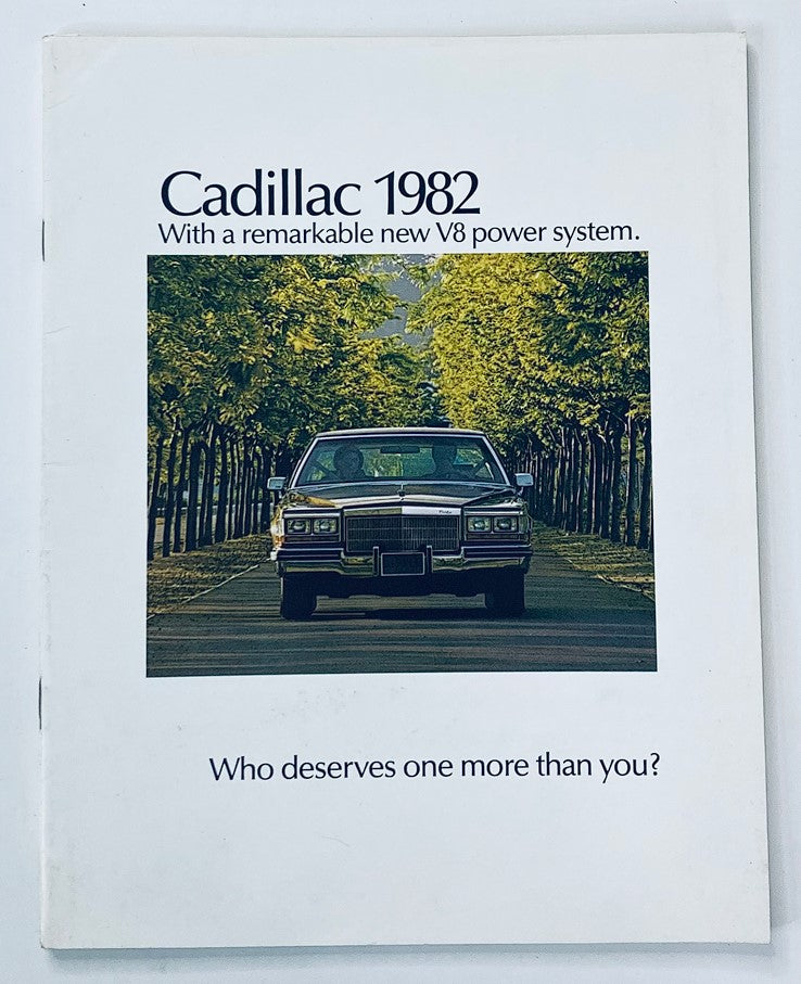 1982 Cadillac V8 Power System Dealer Showroom Sales Brochure featuring a Cadillac car driving through tree-lined street, emphasizing the new V8 power system with the slogan 'Who deserves one more than you?'