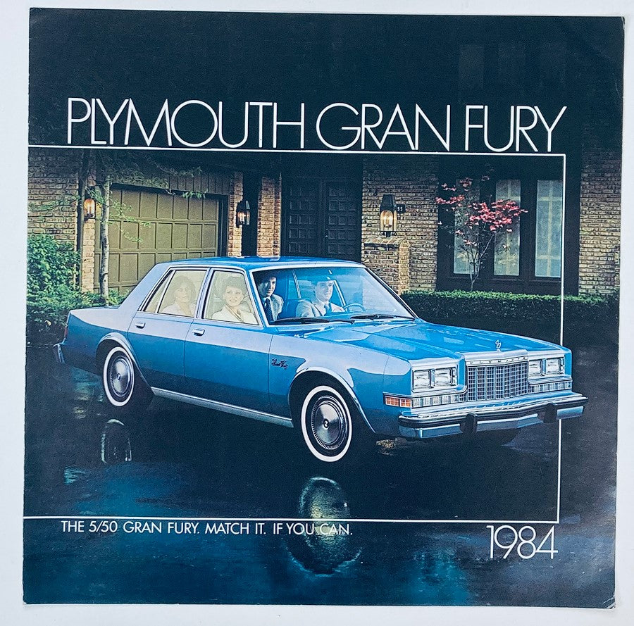 1984 Plymouth Gran Fury Dealer Showroom Sales Brochure Guide Catalog featuring a blue Plymouth Gran Fury car parked in front of a stylish home with two people inside, showcasing the vehicle's design and appeal.