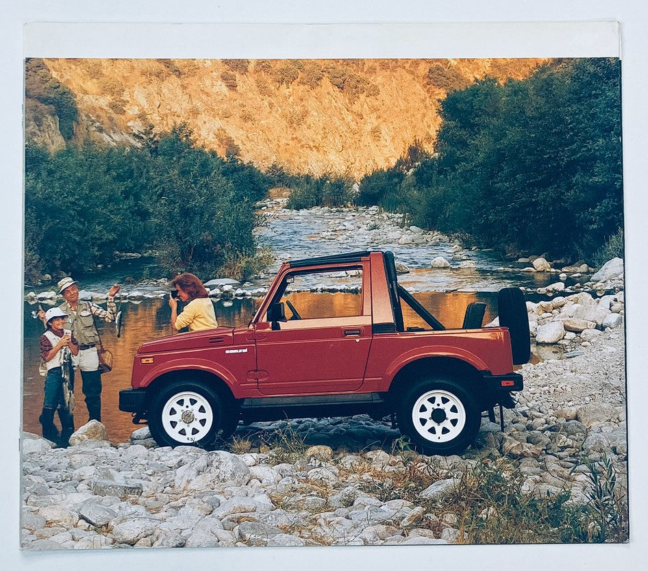 1980s Suzuki SJ Dealer Showroom Sales Brochure Guide Catalog featuring a red Suzuki SJ off-road vehicle parked by a scenic river, surrounded by lush greenery and rocky terrain.