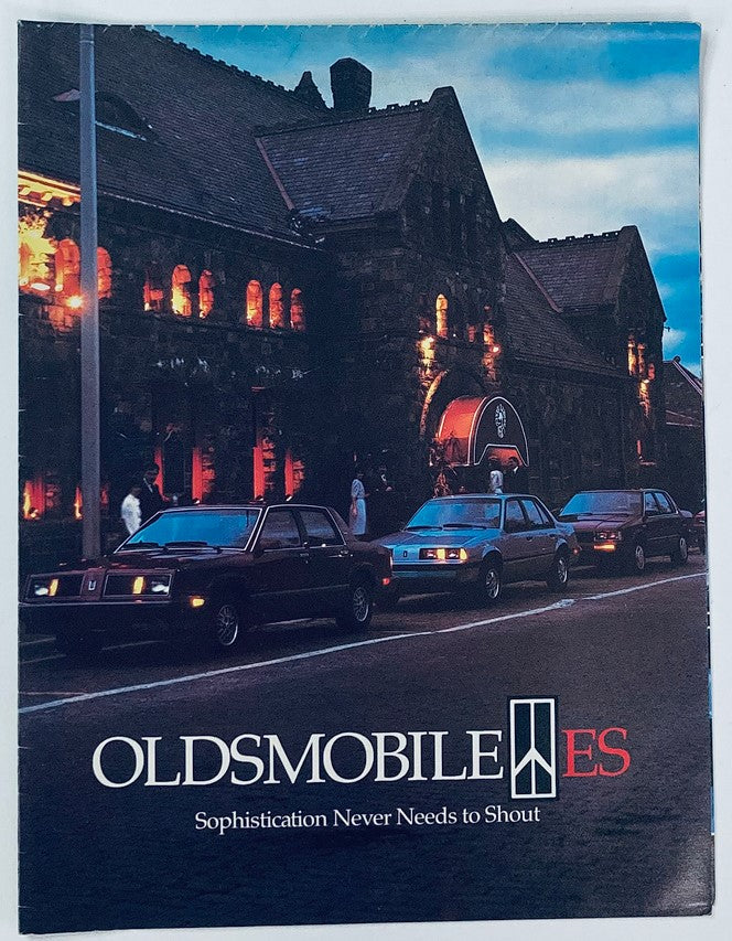 1984 Oldsmobile ES Full Line Dealer Showroom Sales Brochure Guide Catalog featuring a lineup of Oldsmobile vehicles in front of a historic stone building, with the slogan 'Sophistication Never Needs to Shout' prominently displayed.