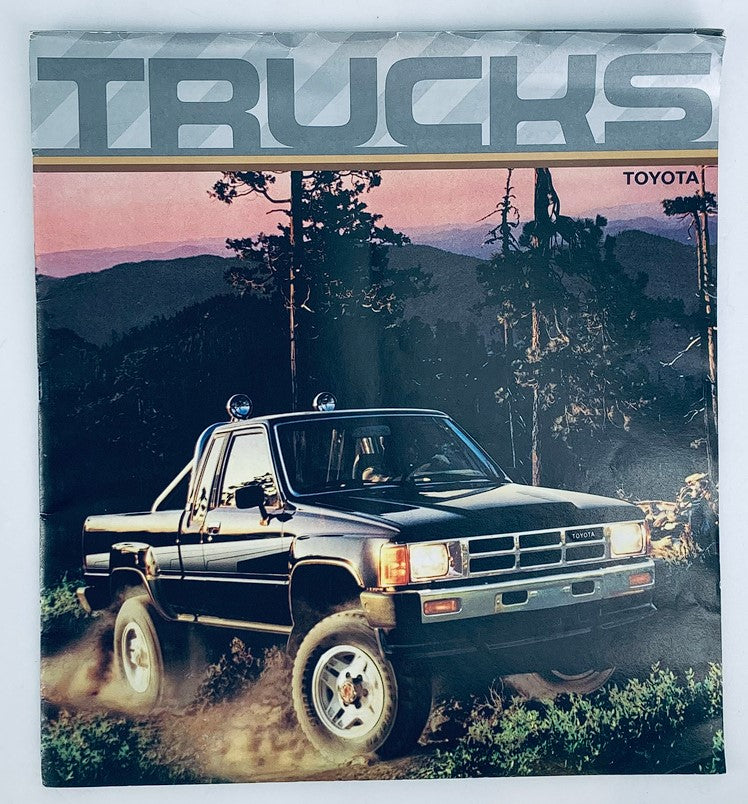 1986 Toyota Trucks Full Line Dealer Showroom Sales Brochure Guide Catalog featuring a black Toyota truck in a scenic outdoor setting against a backdrop of trees and mountains.