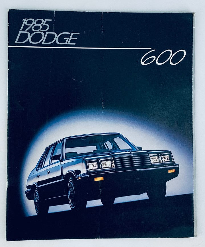 1985 Dodge 600 Lineup Dealer Showroom Sales Brochure featuring a black Dodge 600 car on the front cover, showcasing the vehicle design and branding.