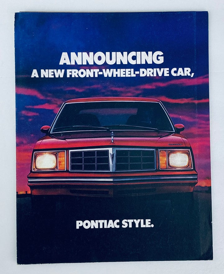 1980 Pontiac Front-Wheel-Drive Dealer Showroom Sales Brochure featuring a front view of a red Pontiac car against a dramatic sunset background with the text 'Announcing A New Front-Wheel-Drive Car, Pontiac Style'.