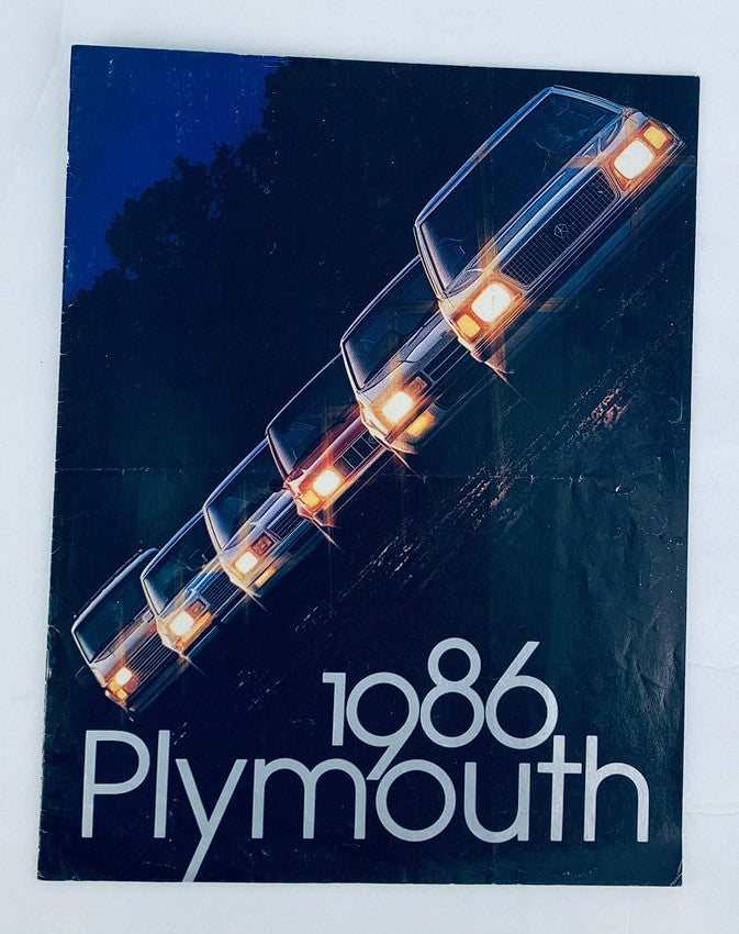 Cover of the 1986 Plymouth Lineup Dealer Showroom Sales Brochure, featuring a lineup of Plymouth vehicles with headlights illuminating the scene, showcasing the brand's offerings in a stylish design.