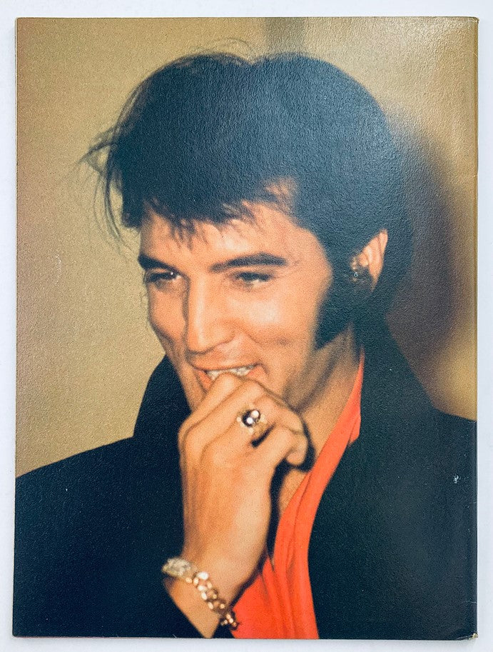 Elvis Presley in a candid moment from the VTG Ideal's Celebrity Series August 1979, showing him smiling thoughtfully while holding his hand to his mouth.