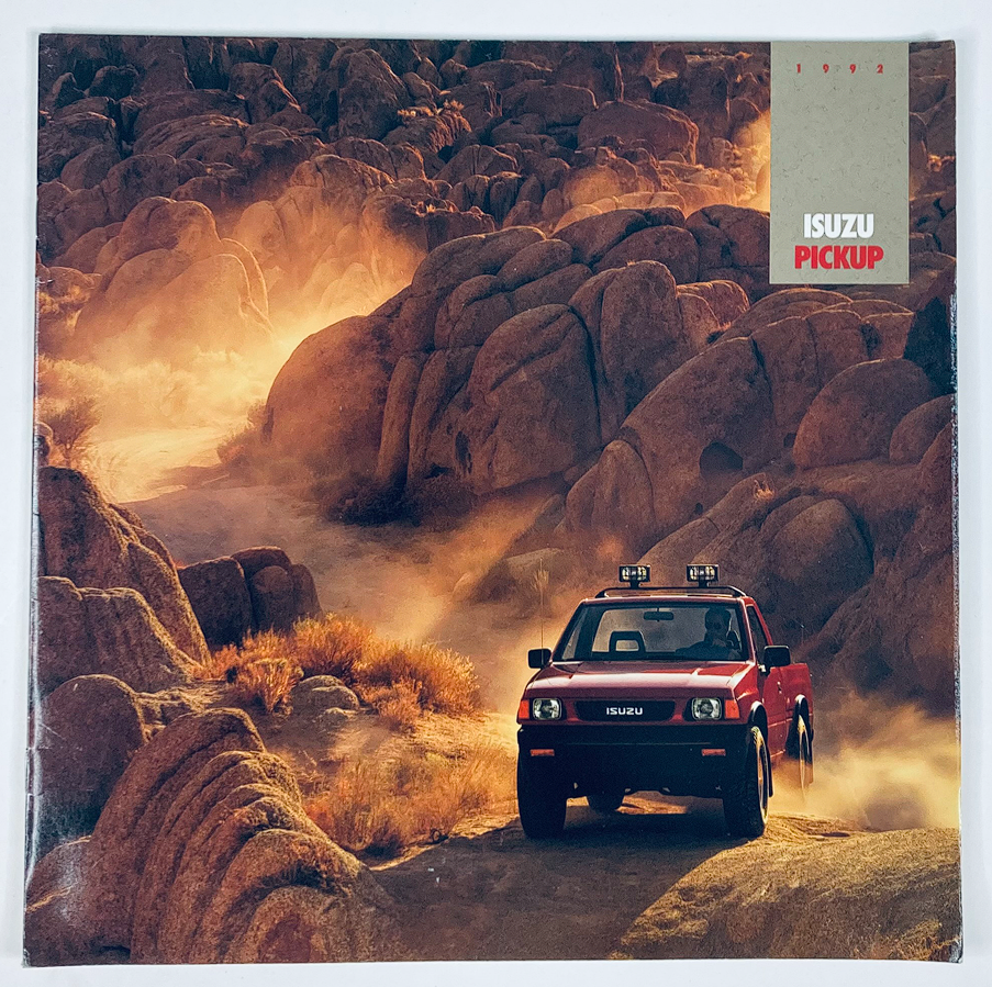1992 Isuzu Pickup Lineup Dealer Showroom Sales Brochure showcasing a red Isuzu pickup truck driving through rocky terrain, highlighting the vehicle's rugged design and outdoor capabilities.