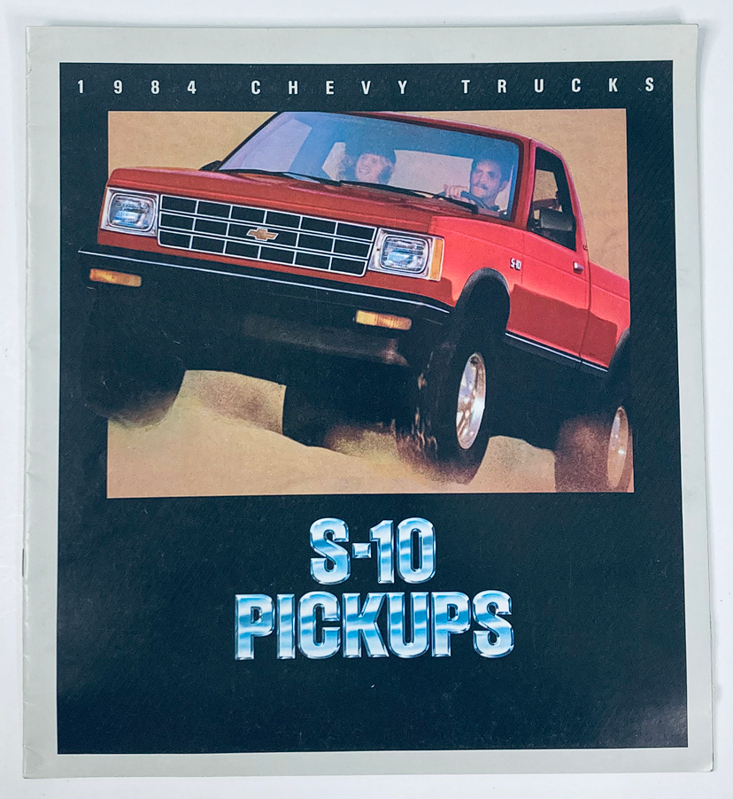 1984 Chevrolet Trucks S-10 Pickups dealer showroom sales brochure featuring a vibrant image of a red S-10 Pickup truck with two passengers, emphasizing the vehicle's design and appeal.