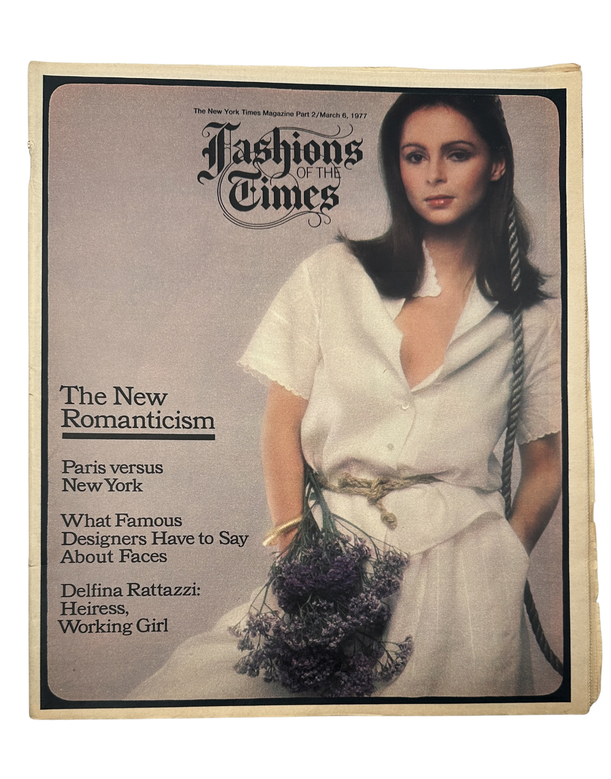 Cover of The New York Times Magazine from March 6, 1977, featuring the title 'The New Romanticism' with themes of Paris versus New York, and highlights on fashion and design. The image showcases a model with long dark hair wearing a white outfit, holding lavender, symbolizing a blend of elegance and contemporary style.