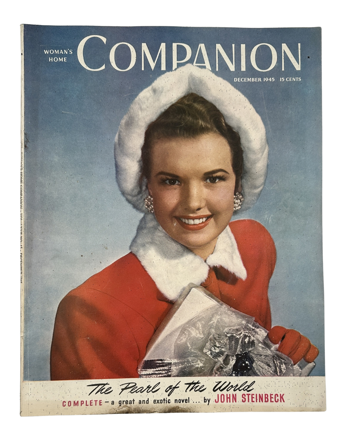 Cover of Woman’s Home Companion Magazine for December 1945, featuring the title 'The Pearl of the World' by John Steinbeck. The cover showcases a smiling woman in a winter outfit with a white fur hat, holding a gift, reflecting a festive holiday theme.