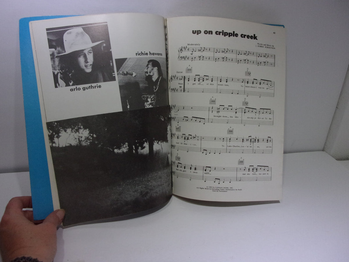 An interior page of the Vintage Woodstock Song Book by Michael Wadleigh, displaying photos of musicians Arlo Guthrie and Richie Havens alongside sheet music for 'Up on Cripple Creek'.