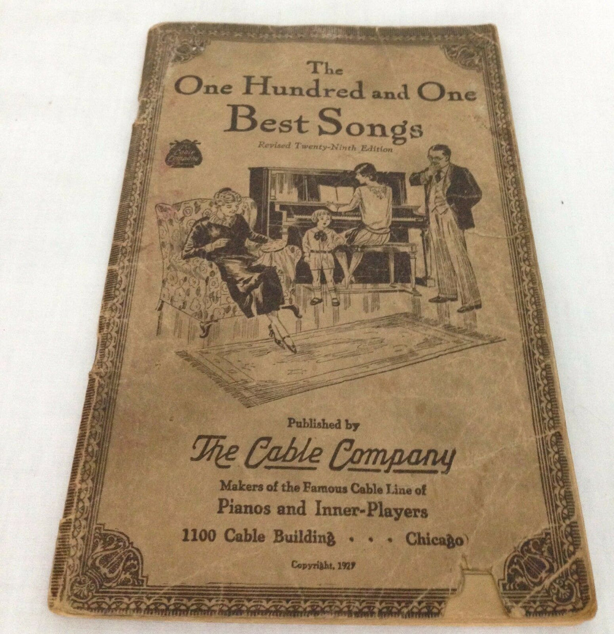 Cover of The One Hundred and One Best Songs, 29th edition, 1927, featuring an illustration of a family gathering by a piano published by The Cable Company.