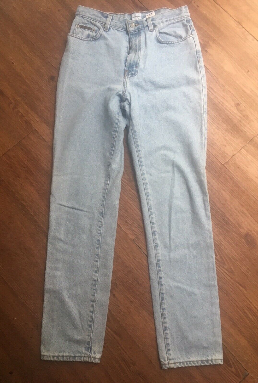 Vintage 90s Calvin Klein High Rise Mom Jeans Light Blue Denim Straight Leg Sz. 8 displayed on wooden floor, showcasing the stylish high rise and straight leg fit.