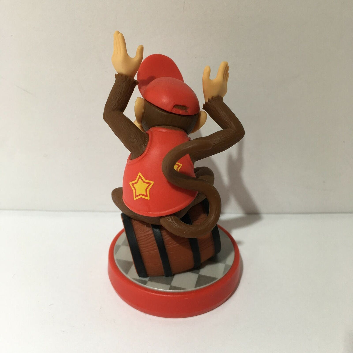 Back view of Nintendo Amiibo Diddy Kong figurine showcasing Diddy Kong wearing a red cap and vest, seated on a barrel base. Perfect for collectors and gaming enthusiasts.