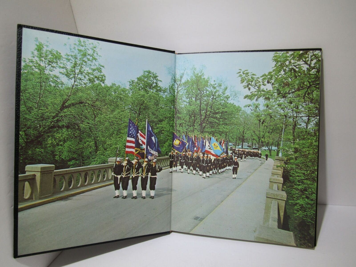 Photo from the Vintage 1966 Keel United States Naval Training Center Company 1 yearbook depicting a marching formation with flags among greenery, representing the pride and discipline of naval trainees.