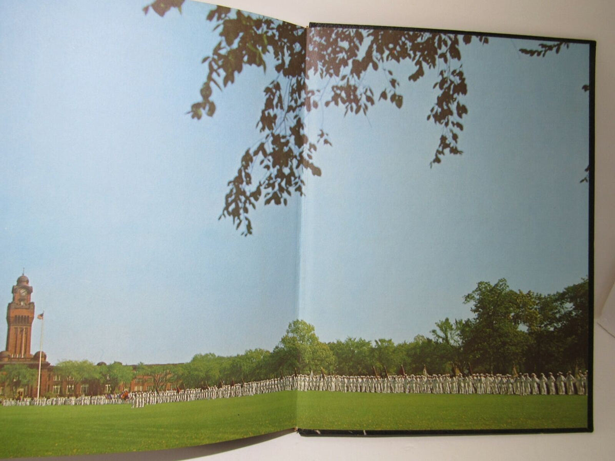 Image from the Vintage 1966 Keel United States Naval Training Center Company 1 yearbook showing a large group of naval recruits in formation on a grassy field with a historic clock tower in the background.