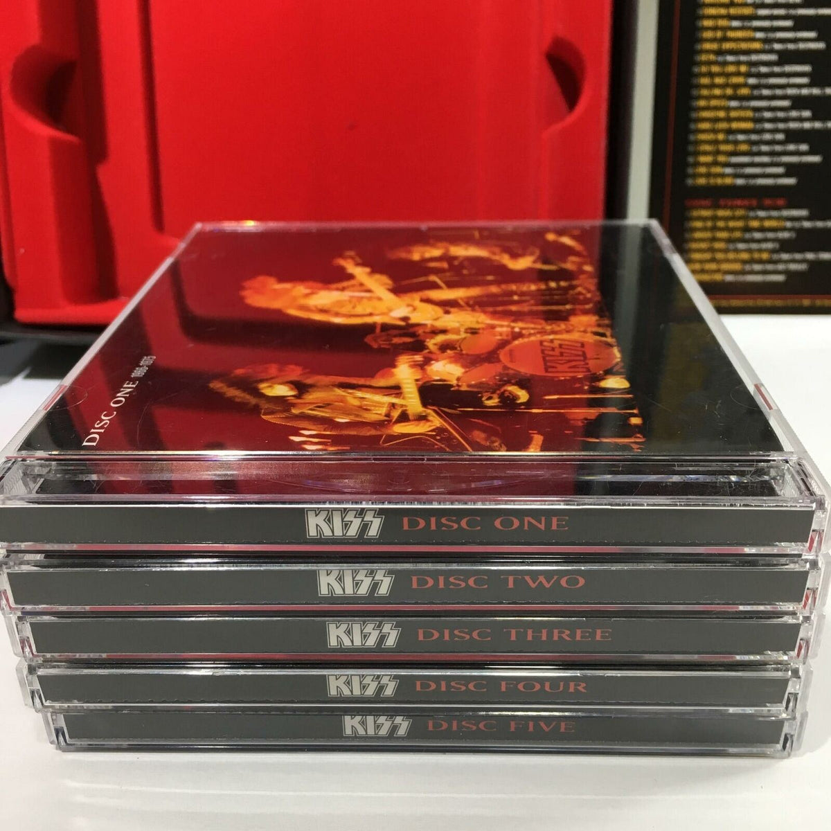 Definitive Kiss Collection 5 Disc Box Set with Booklet - Close-up of five audio CDs stacked, each labeled with their respective disc number, set against a red and black background.